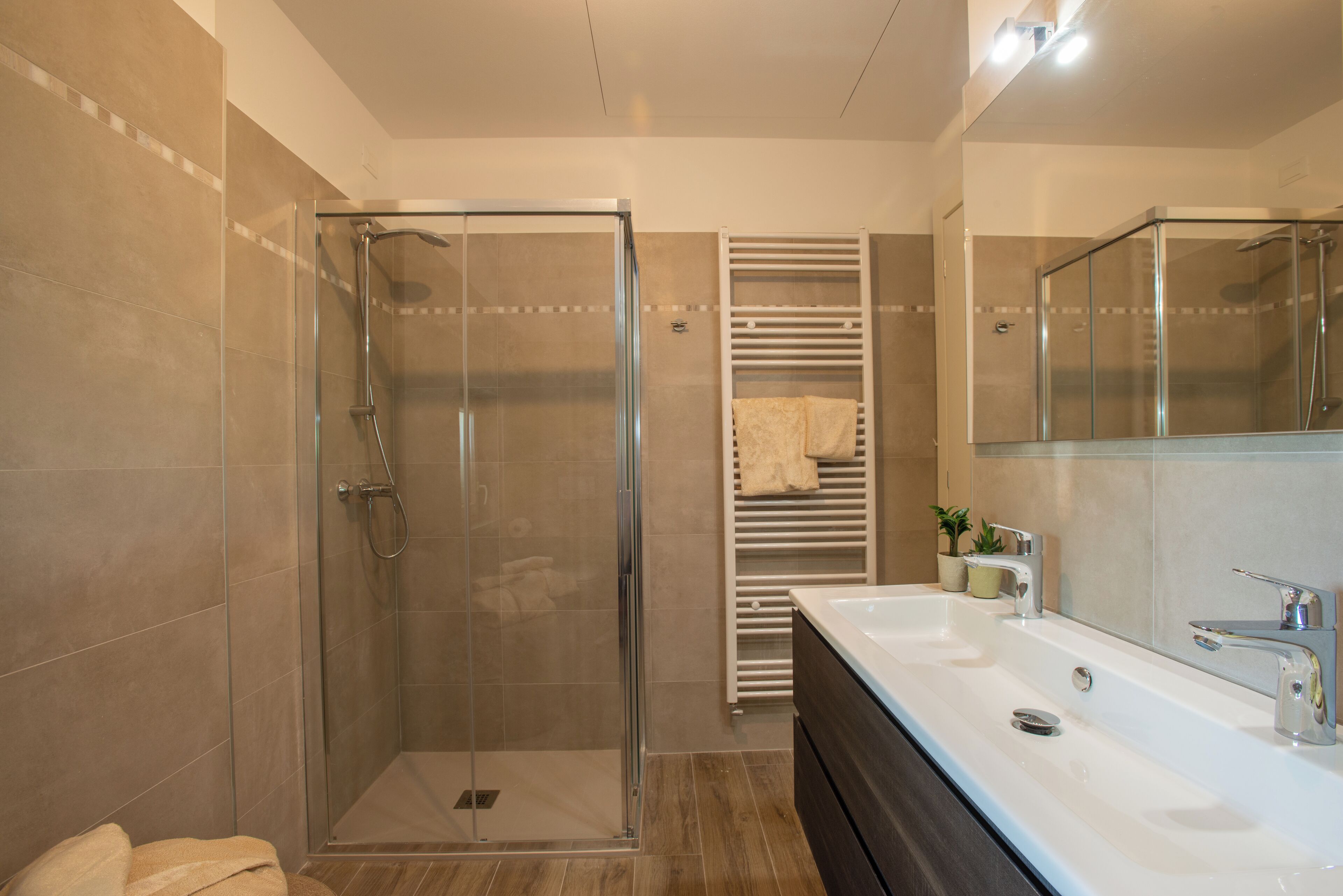 Une salle de bain moderne avec une douche à parois de verre, un grand lavabo avec un miroir et un porte-serviettes.