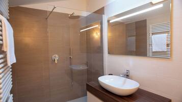 Ein modernes Badezimmer mit einer Glastrennwand zur Dusche, einem weißen Waschbecken und einem Holzwaschtisch.