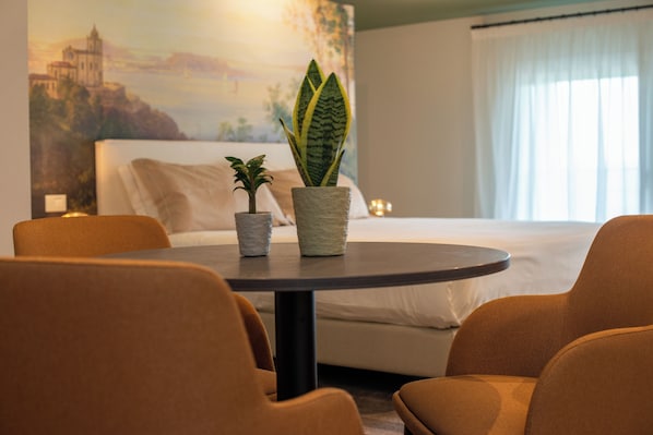Una habitación de hotel con cama, una mesa redonda con sillas y dos plantas en macetas.