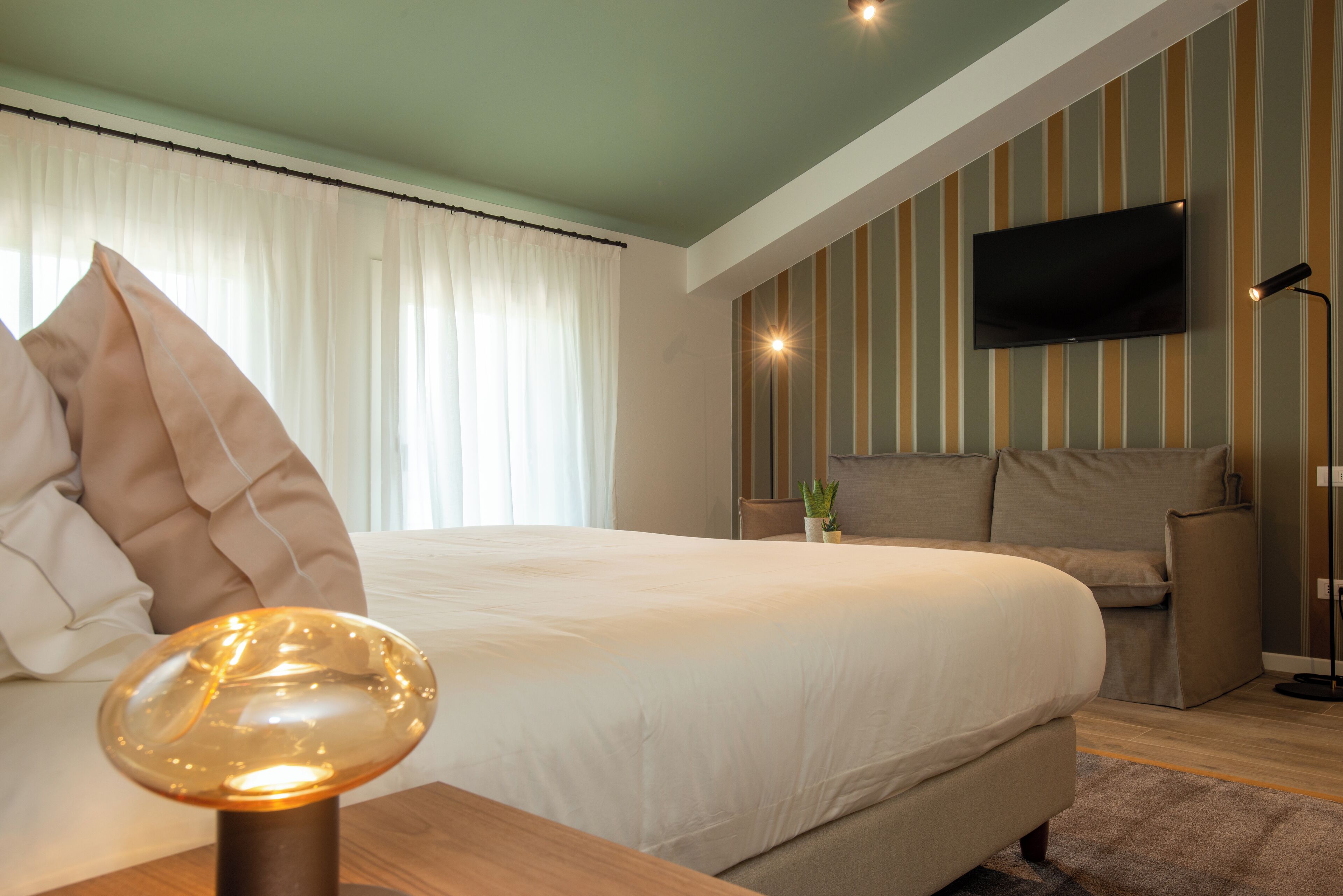 Une chambre d’hôtel moderne dotée d’un grand lit, d’un téléviseur à écran plat fixé au mur et d’une table de chevet avec une lampe.