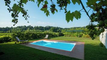 Une piscine rectangulaire avec une terrasse en bois, entourée d’une pelouse bien entretenue et offrant une vue sur une zone boisée.
