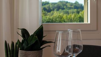 A table with two wine glasses and a potted plant by a window with a view of greenery.