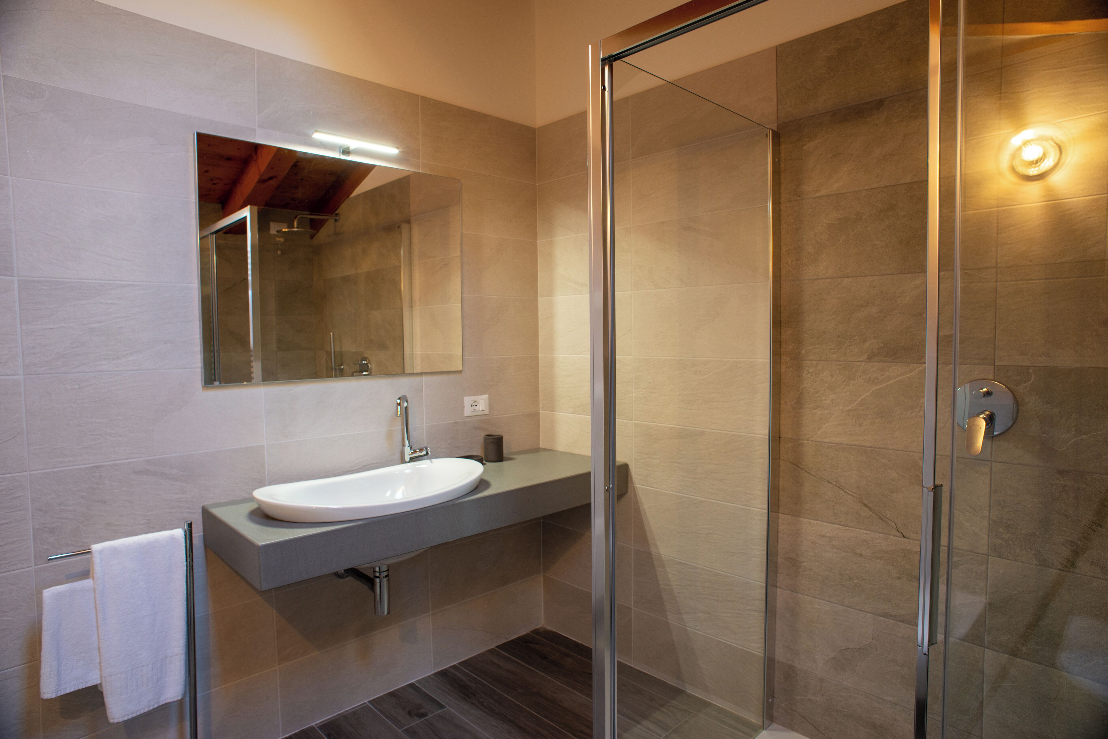 Un baño moderno con ducha envuelta en vidrio, lavamanos integrado y un espejo grande.