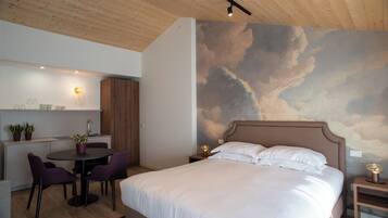 A bedroom with a large bed, a dining area with chairs and a table, and a wall with a cloud mural.
