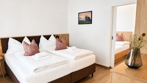 Cama de casal com almofadas brancas e cor-de-rosa, cabeceira de madeira e mesa de cabeceira com um vaso.