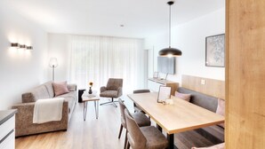 Uma sala de estar moderna com um sofá, uma mesa de jantar e uma mesa de centro. Há uma luminária, um porta-retrato e uma janela com cortinas.