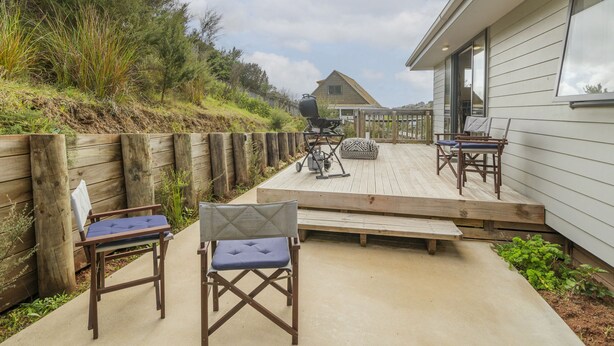 Eine Holzterrasse mit Gartenmöbeln, einem Grill und Blick auf ein Haus im Hintergrund.