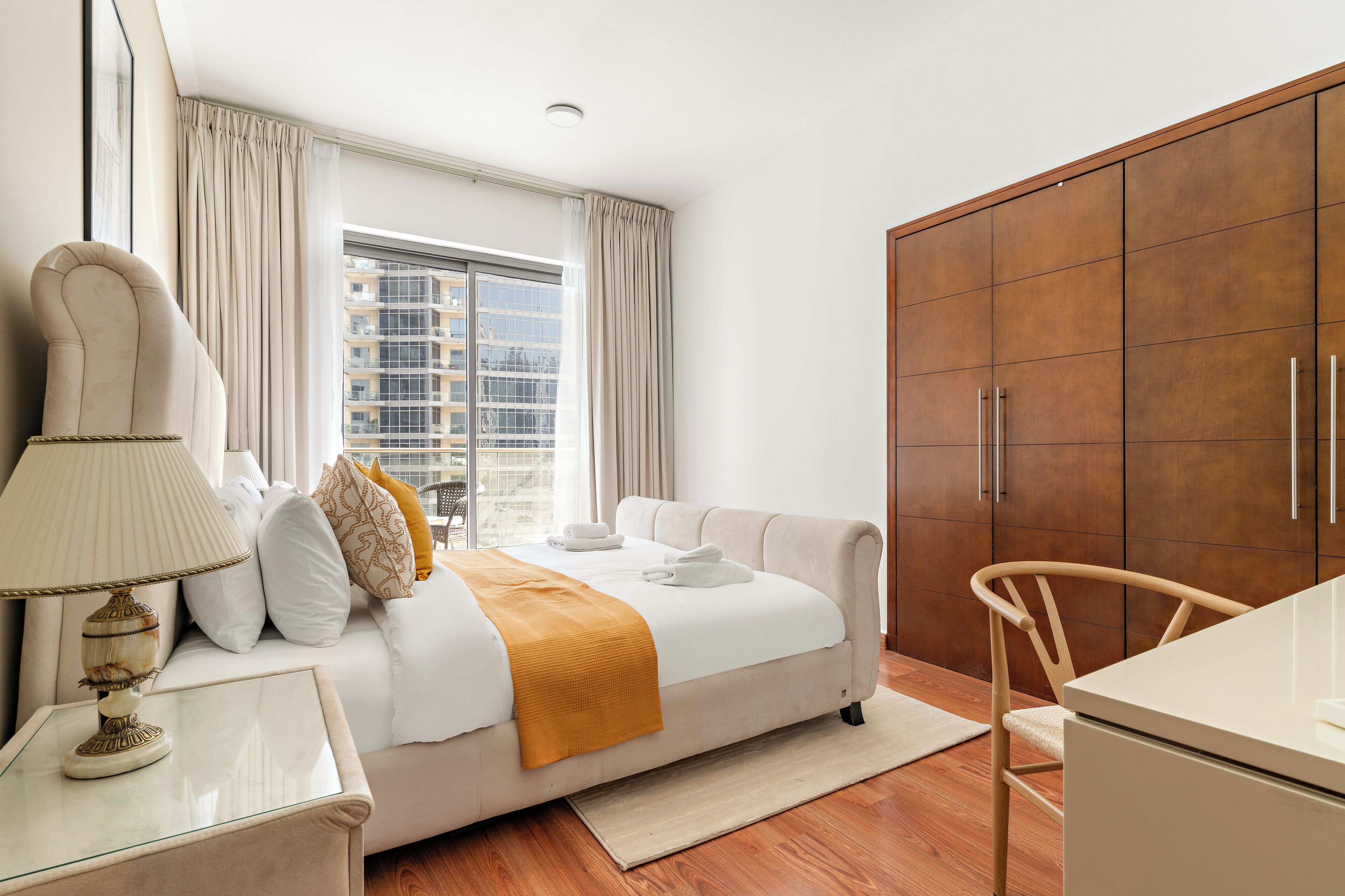 Habitación de hotel con una cama grande, un escritorio, una silla, un armario y una ventana con cortinas.