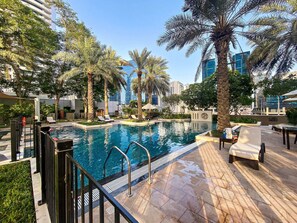 A swimming pool with lounge chairs and palm trees, surrounded by modern buildings.