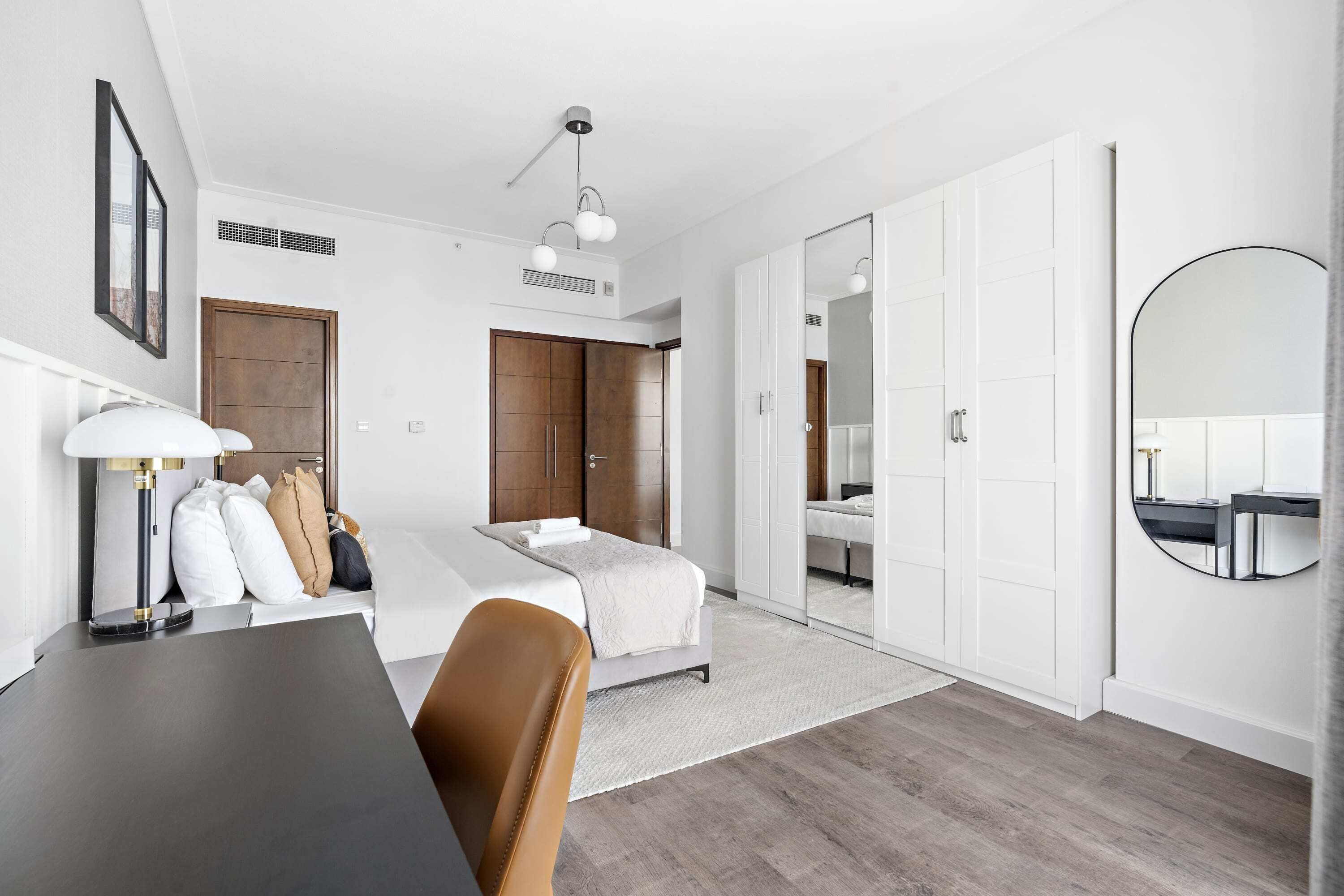 Ein modernes Hotelzimmer mit einem Bett, einem Schreibtisch und einem Sessel. Ein Kleiderschrank und ein Spiegel sind an der Wand angebracht.