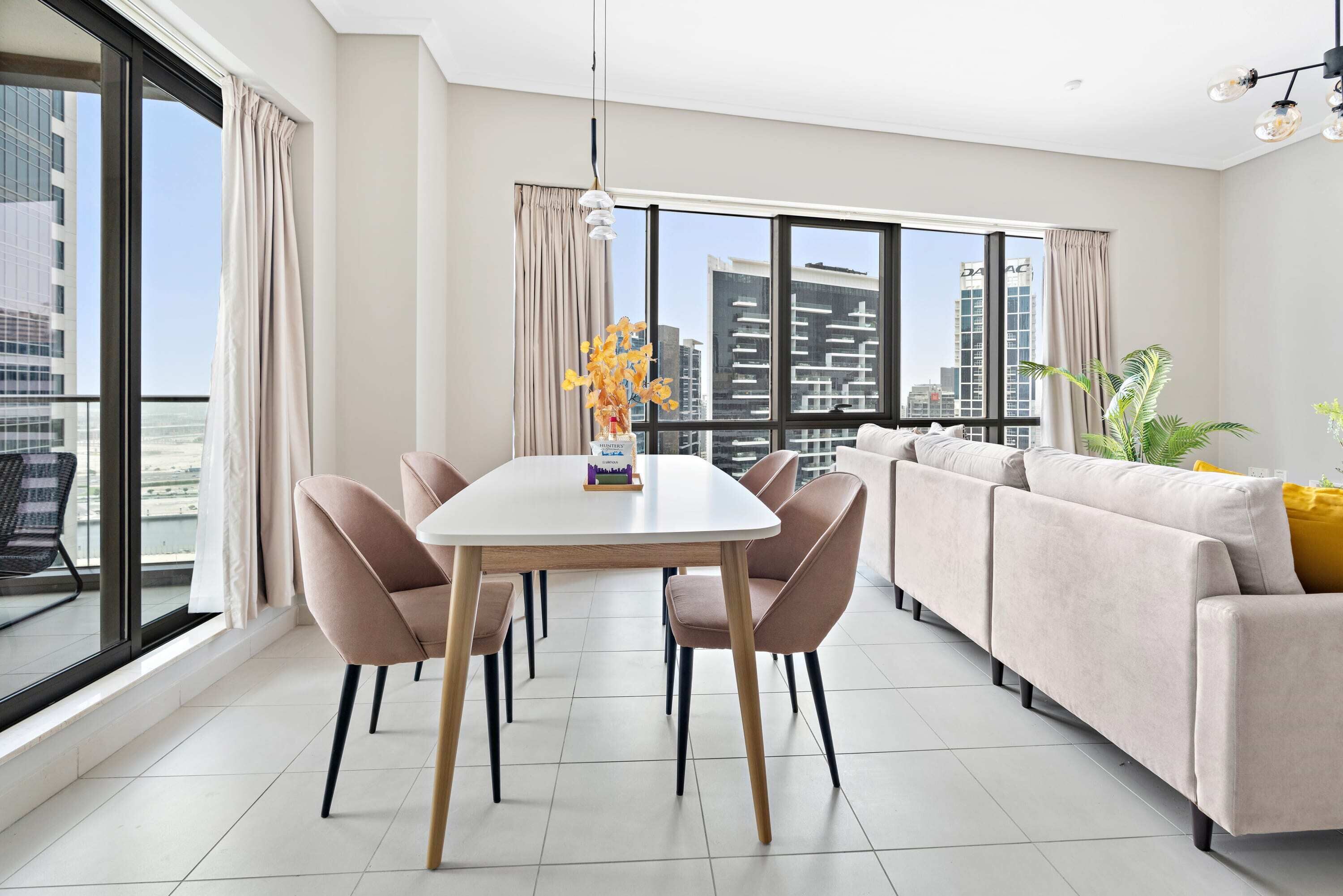A modern living room with a dining table, sofa, and large windows offering a city view.