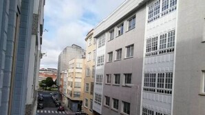 En smal gade i byen med høje bygninger, parkerede biler og et fodgængerfelt.