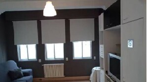 En stue med en blå sofa, en radiator og et fjernsyn på et skab.