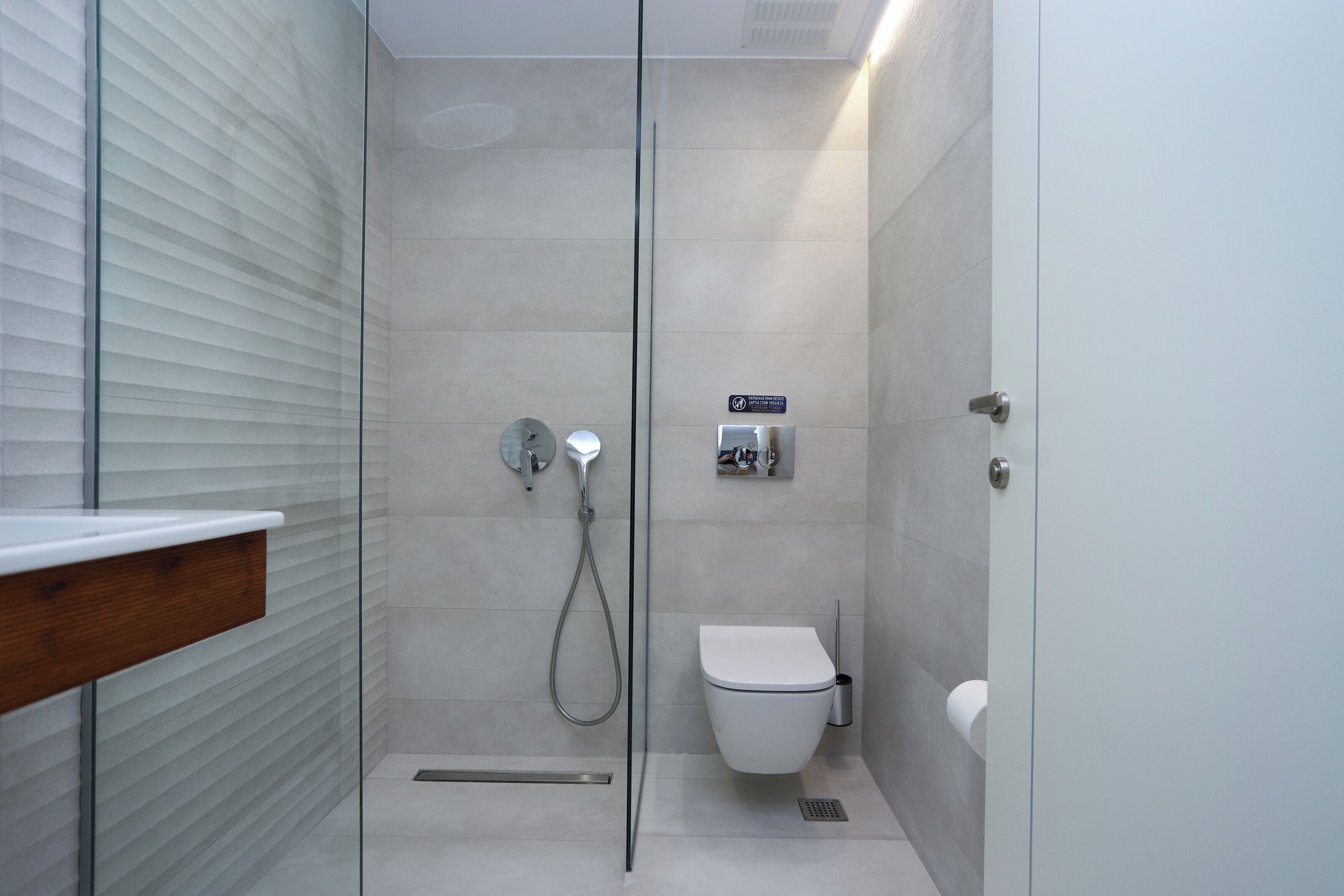 A modern bathroom with a glass shower enclosure, a toilet, and a hand dryer.