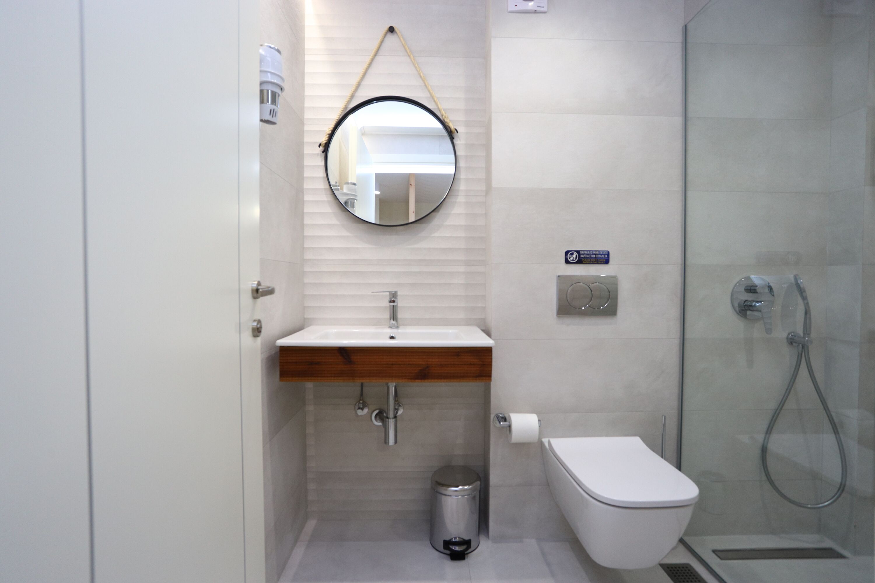 A modern bathroom with a round mirror, white sink, toilet, and glass shower enclosure.