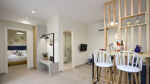 A modern kitchen with white bar stools, a wooden dining table, and a built-in shelf with decorative items. - ONAR OURANOUPOLIS (Aristotelis)