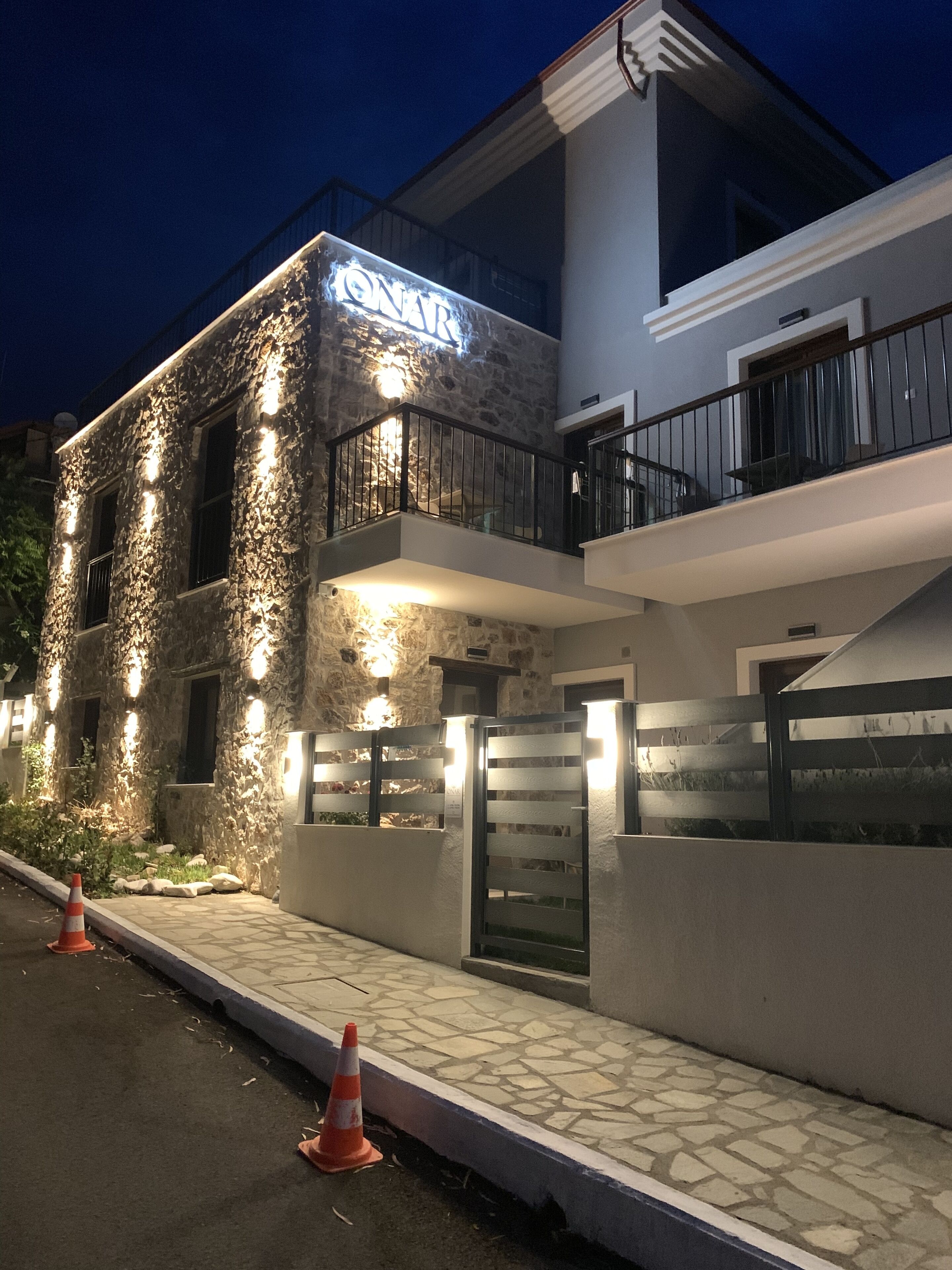 A building with a stone facade, a balcony with a black railing, and a sign that reads "ONAT".