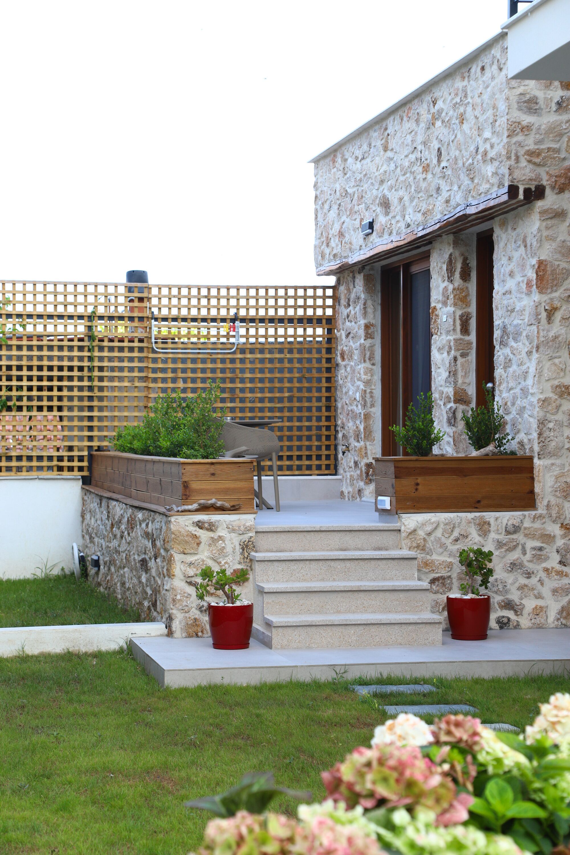 A stone building with a wooden staircase leading to a door, potted plants, and a grassy area.