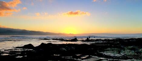 A rocky shoreline with a sunset in the background.