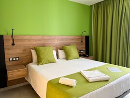 Camera d'albergo con testiera in legno, pareti verdi, un letto grande con biancheria da letto bianca e tocchi di verde, un comodino con un telefono e una presa di corrente, e una tenda verde.