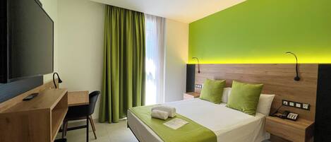 A hotel room with a bed, bedside table, lamp, desk, chair, and a television.