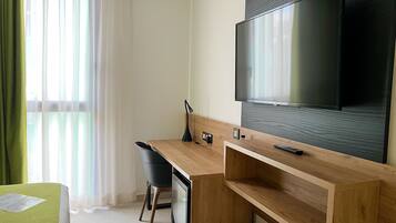 Ett modernt hotellrum med ett skrivbord i trä, en tv som är monterad på väggen, en stol och en säng med ett grönt överdrag.