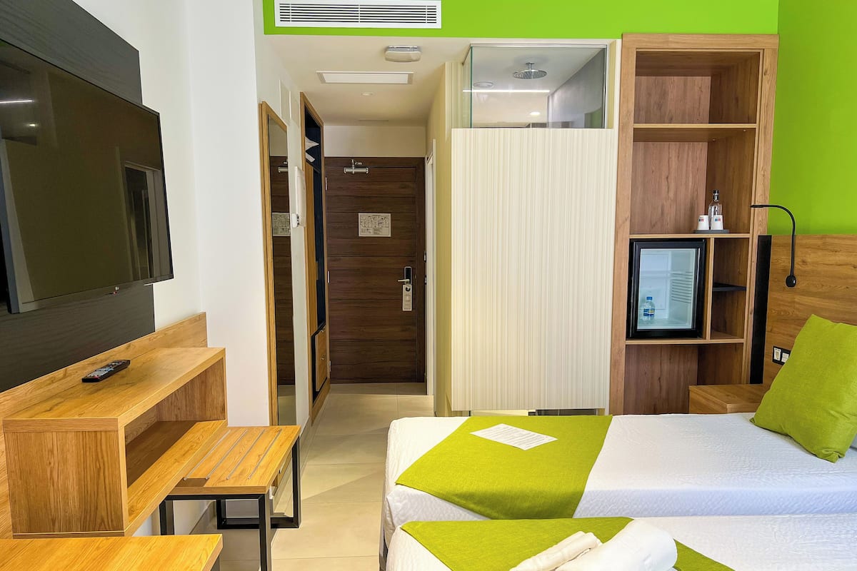 A hotel room with a bed, a desk, a TV, a bathroom, and a shelf with toiletries.