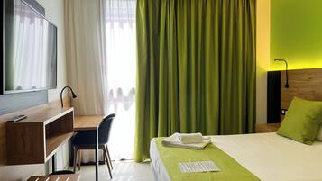 Ein Hotelzimmer mit Bett, Schreibtisch, Sessel, Fernseher und einem fensterbepflanzten Fenster.