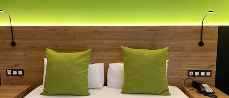 A hotel room with a wooden headboard, two green pillows, a white bedspread, and a bedside table with a phone.