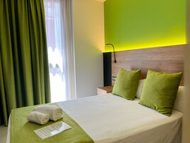 A hotel room with a neatly made bed, green curtains, and a wooden headboard.
