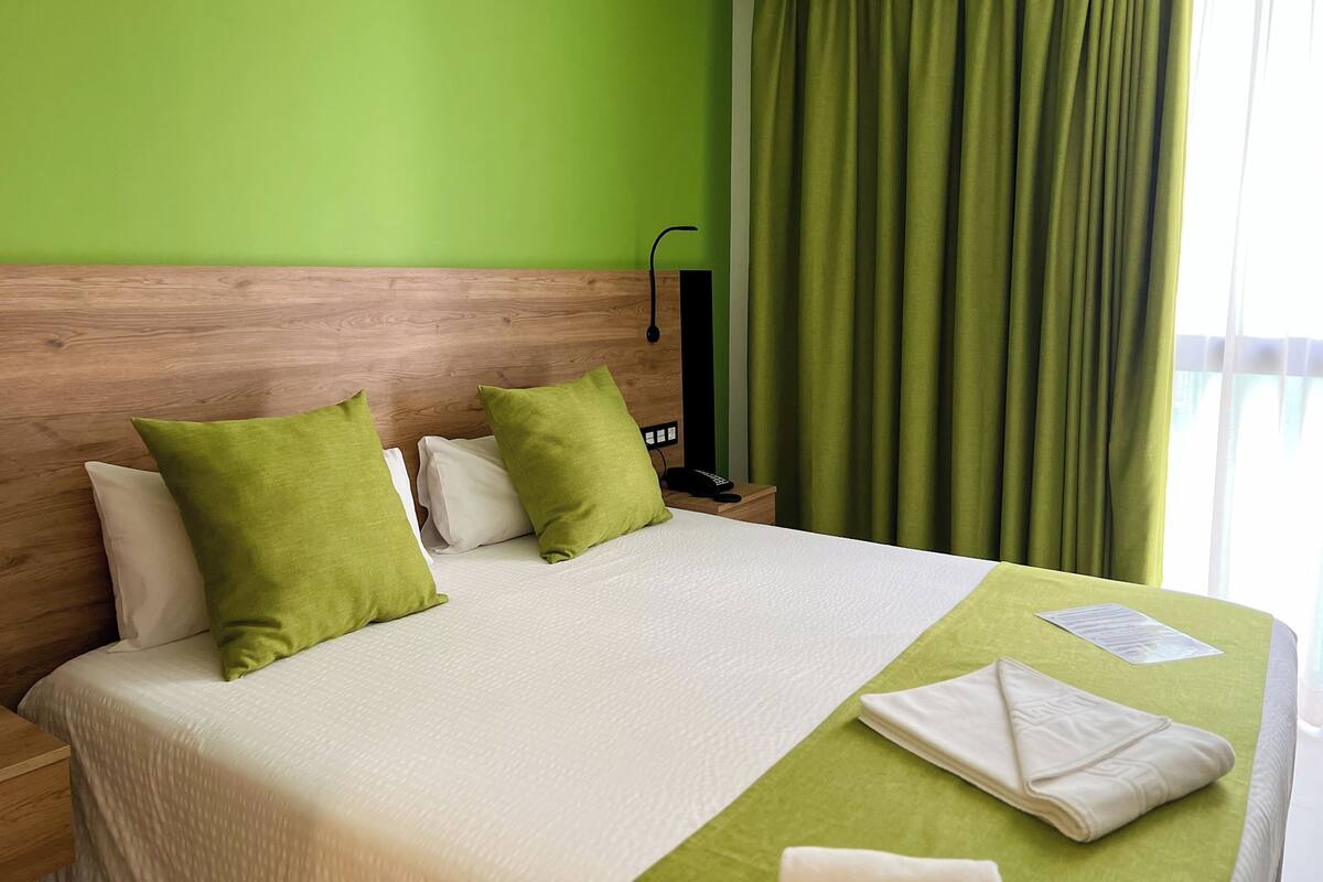 A hotel room with a wooden headboard, a green wall, and a bed with white bedding and green pillows.