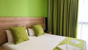 Une chambre d’hôtel avec une tête de lit en bois, un mur vert et un lit avec une literie blanche et des oreillers verts.