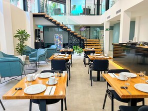 A modern dining area with wooden tables and blue chairs, a staircase, and a reception desk. - Hotel MG Poniente (Las Palmas de Gran Canaria)