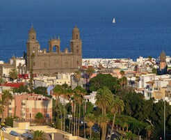 A coastal cityscape with a prominent church featuring two towers and a central dome, surrounded by residential buildings and palm trees.