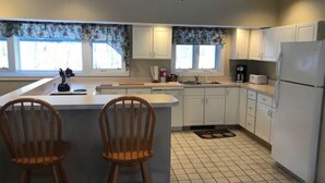 A kitchen with white cabinets, a central island with two wooden chairs, a refrigerator, and a coffee maker. - Penthouse with Mountain Views, Pools & Jacuzzis (Lincoln)