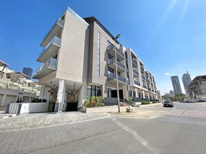 A modern multi-story building with balconies, a paved entrance area, and a clear sky.