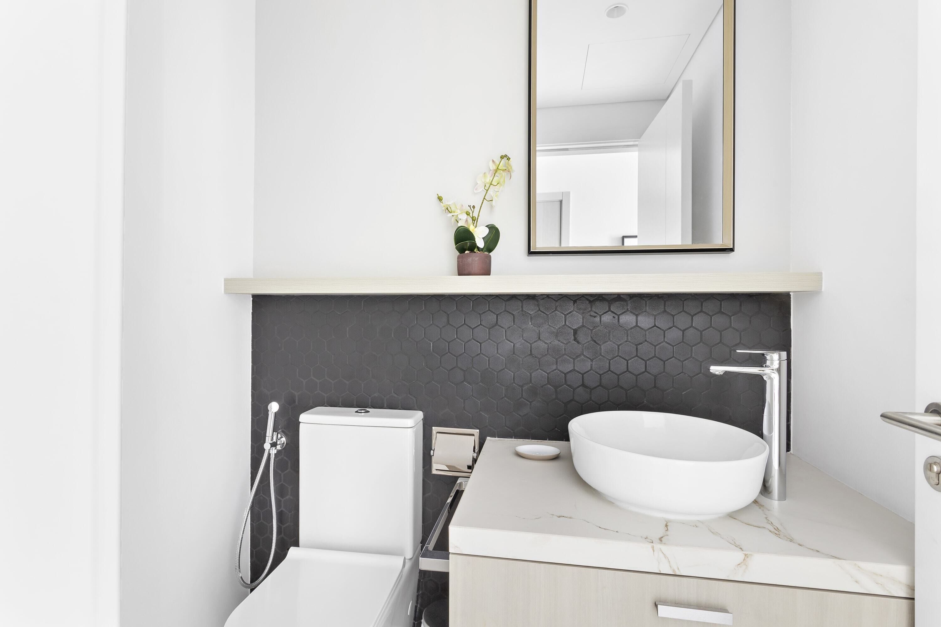 A modern bathroom with a white sink, a mirror, and a potted orchid.