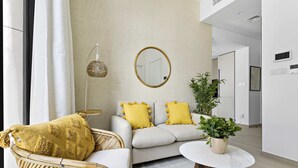 Een moderne woonkamer met een bank, een rieten fauteuil, een ronde salontafel en een potplant.