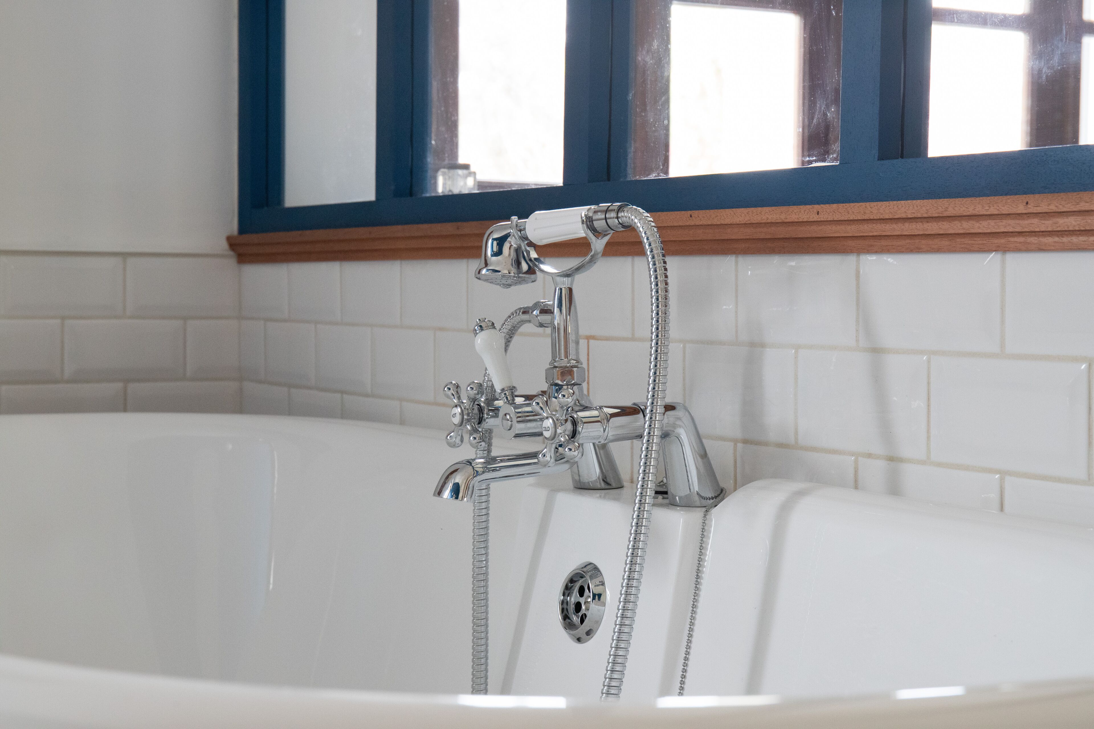 Een badkamer met een wit bad, chroombeslag en een raam met blauwe omlijsting.