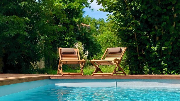 A clear swimming pool with two wooden lounge chairs and lush greenery in the background. - Maison et table d'hôtes le Camélia Blanc (Saint-Ciers-sur-Gironde)