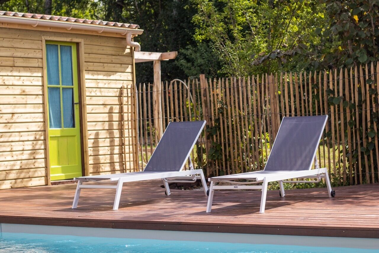 Terraza de madera con dos sillones blancos y una piscina.