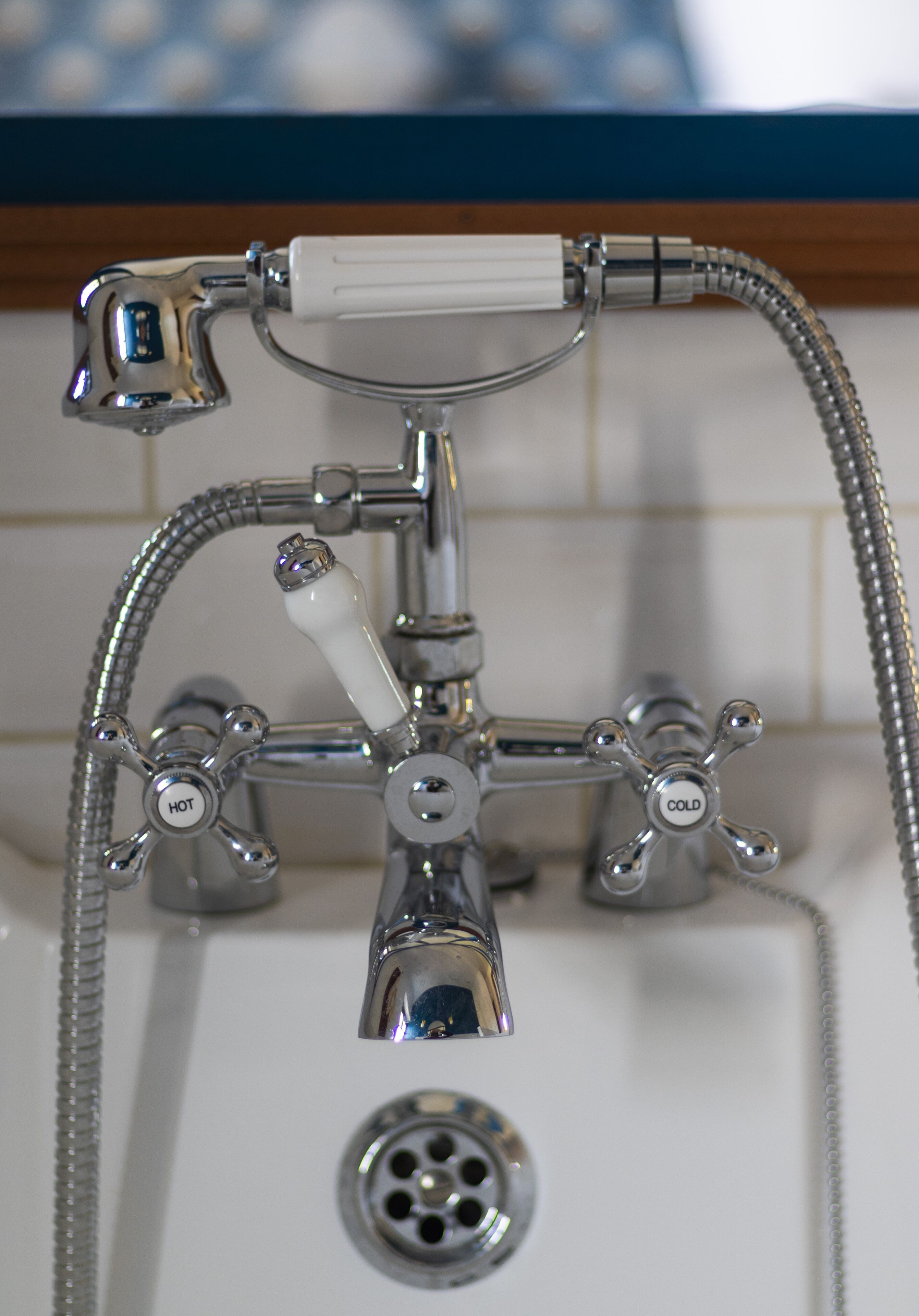 A bathroom with a chrome faucet, a shower head, and a drain.