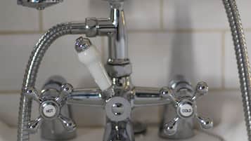A bathroom with a chrome faucet, a shower head, and a drain.