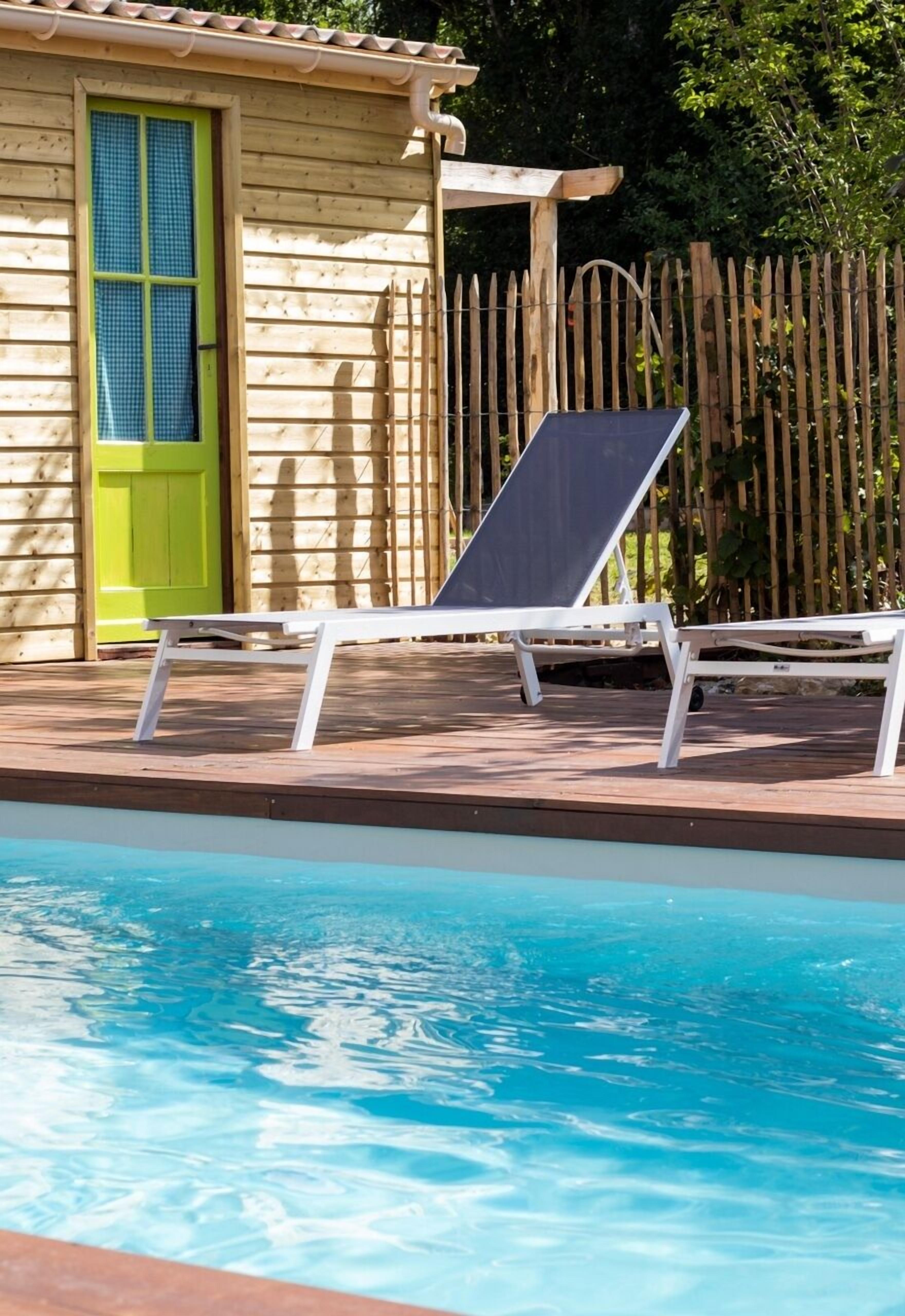 Ein Poolbereich mit Holzterrasse, einem weißen Liegestuhl und einer grünen Tür.