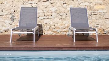 Deux chaises longues placées près d’une piscine, avec un mur de pierres en arrière-plan.
