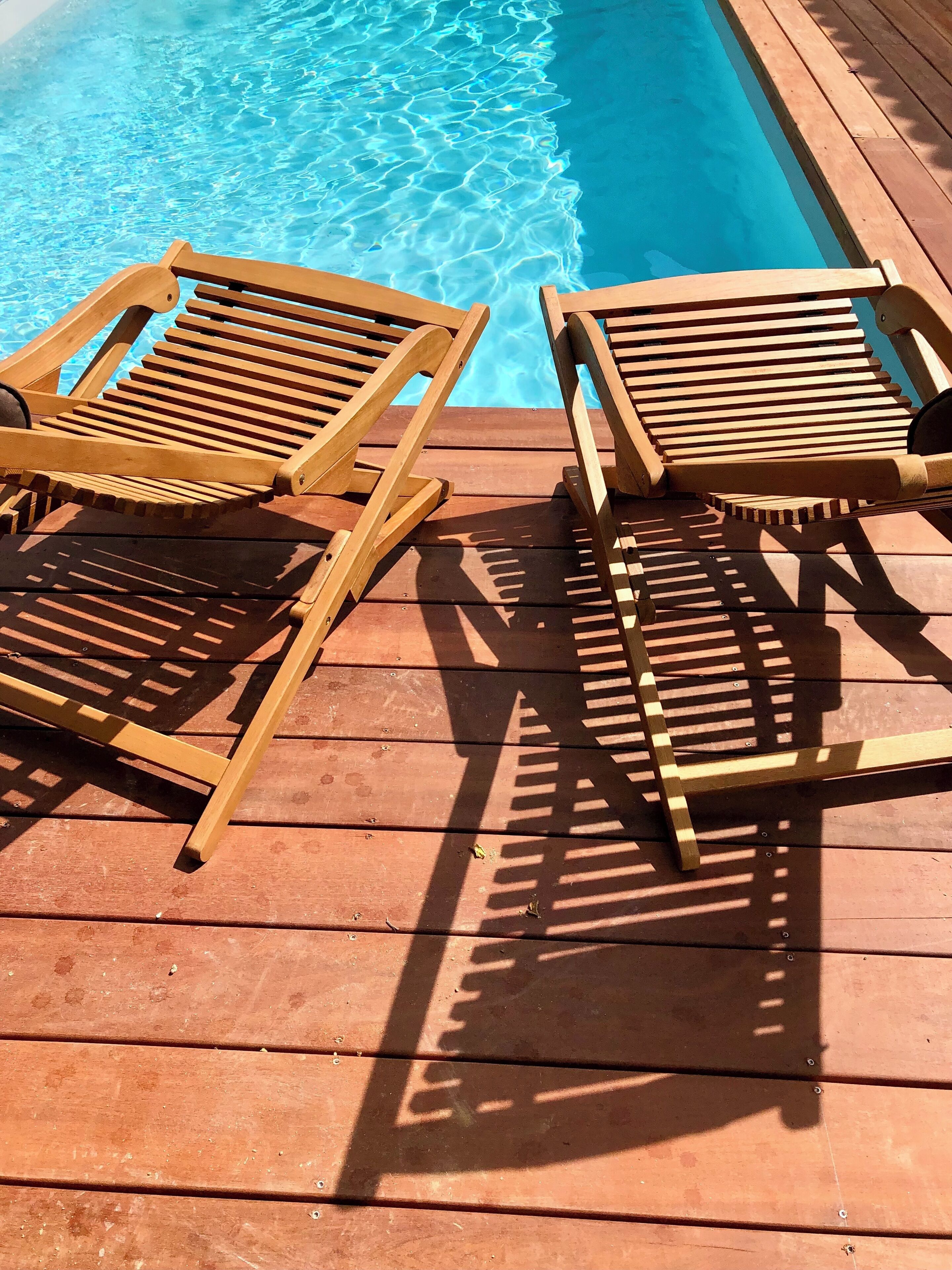 Une terrasse en bois avec deux chaises longues et une table, située près d’une piscine.