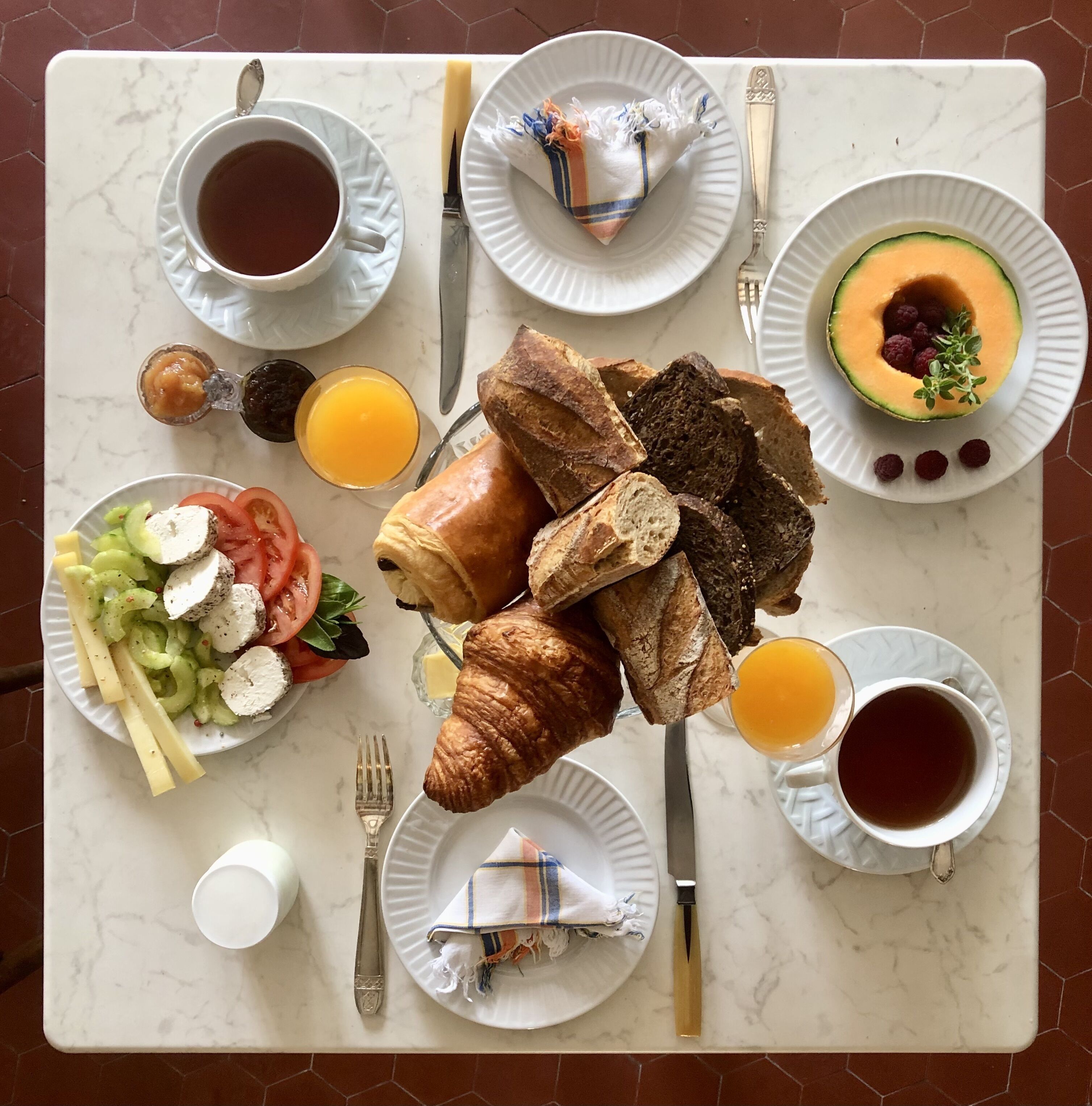 Een ontbijttafel met croissants, brood, fruit en drankjes.