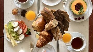 A breakfast table with croissants, bread, fruit, and beverages.