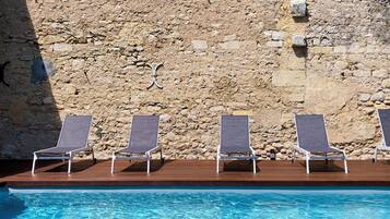 Zona de piscina con cuatro sillones de descanso y un muro de piedra al fondo.