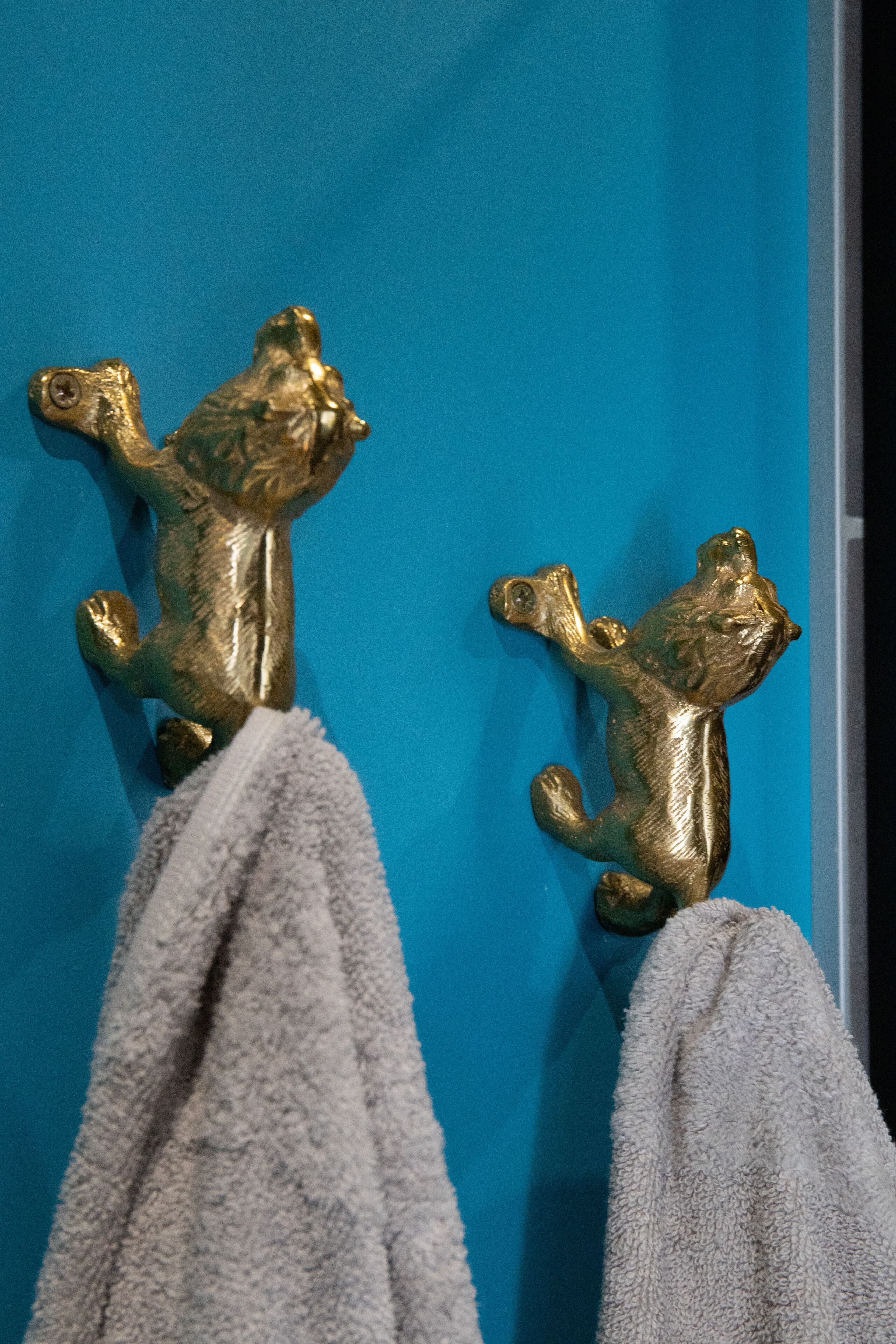 Dos ganchos en forma de animales dorados sobre una pared azul.